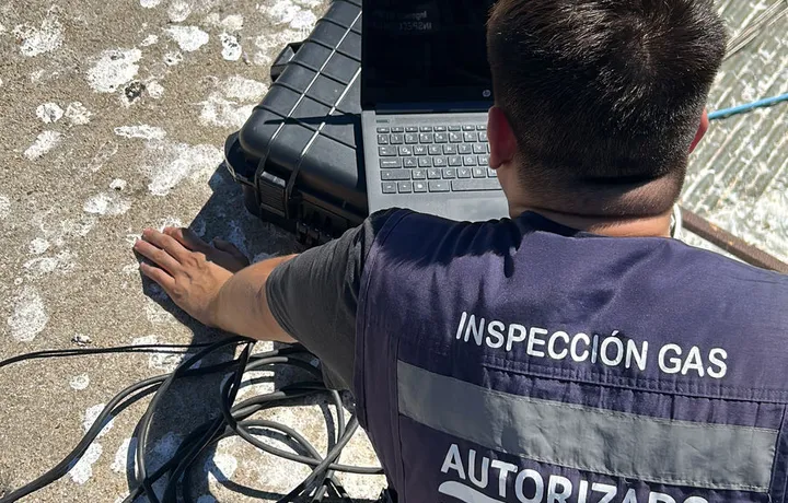 Inspector de Ingeniería RS, de espaldas y con chaleco de inspección de gas, trabajando con su computador en la azotea de un edificio