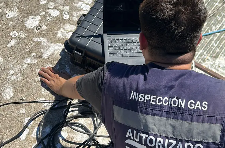 Inspector de Ingeniería RS, de espaldas y con chaleco de inspección de gas, trabajando con su computador en la azotea de un edificio